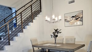 Un espace repas comprenant une table en bois, des chaises rembourrées, un banc, un lustre et un escalier.