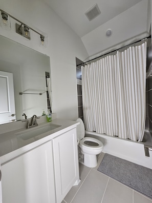 A bathroom with a white sink, a toilet, a shower curtain, and a mirror. - Songbird Luxury Retreat — a Modern 4BR Getaway in Wylie, Near Lake Lavon (Wylie)