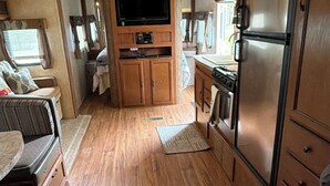 A compact RV interior with a kitchenette, a flat-screen TV, and a dining area.
