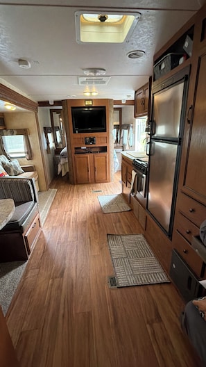 A compact RV interior with a kitchenette, a flat-screen TV, and a dining area.