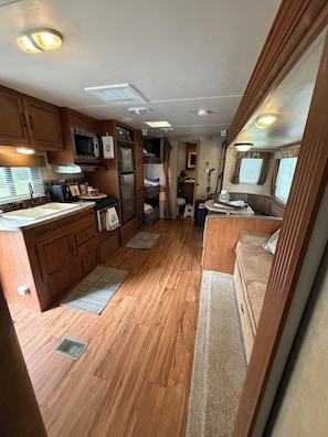 Une cuisine compacte pour camping-car, dotée de meubles en bois, d’un four à micro-ondes, d’un réfrigérateur et d’un petit coin repas avec une banquette.