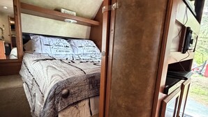 A bedroom with a bed, a wooden wardrobe, and a small desk with a chair.