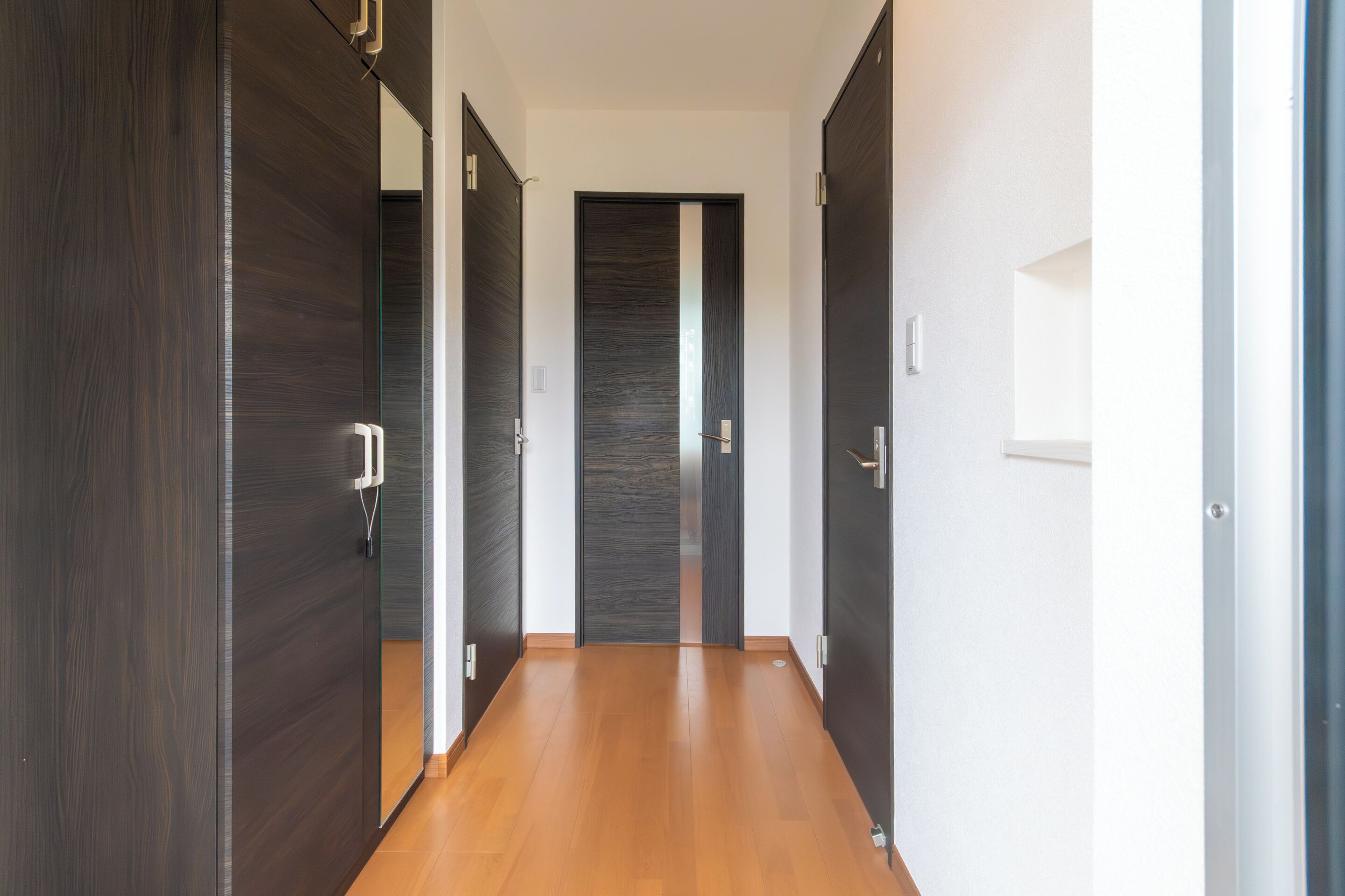 Un pasillo con puertas de madera oscura, piso de color claro y pared blanca.