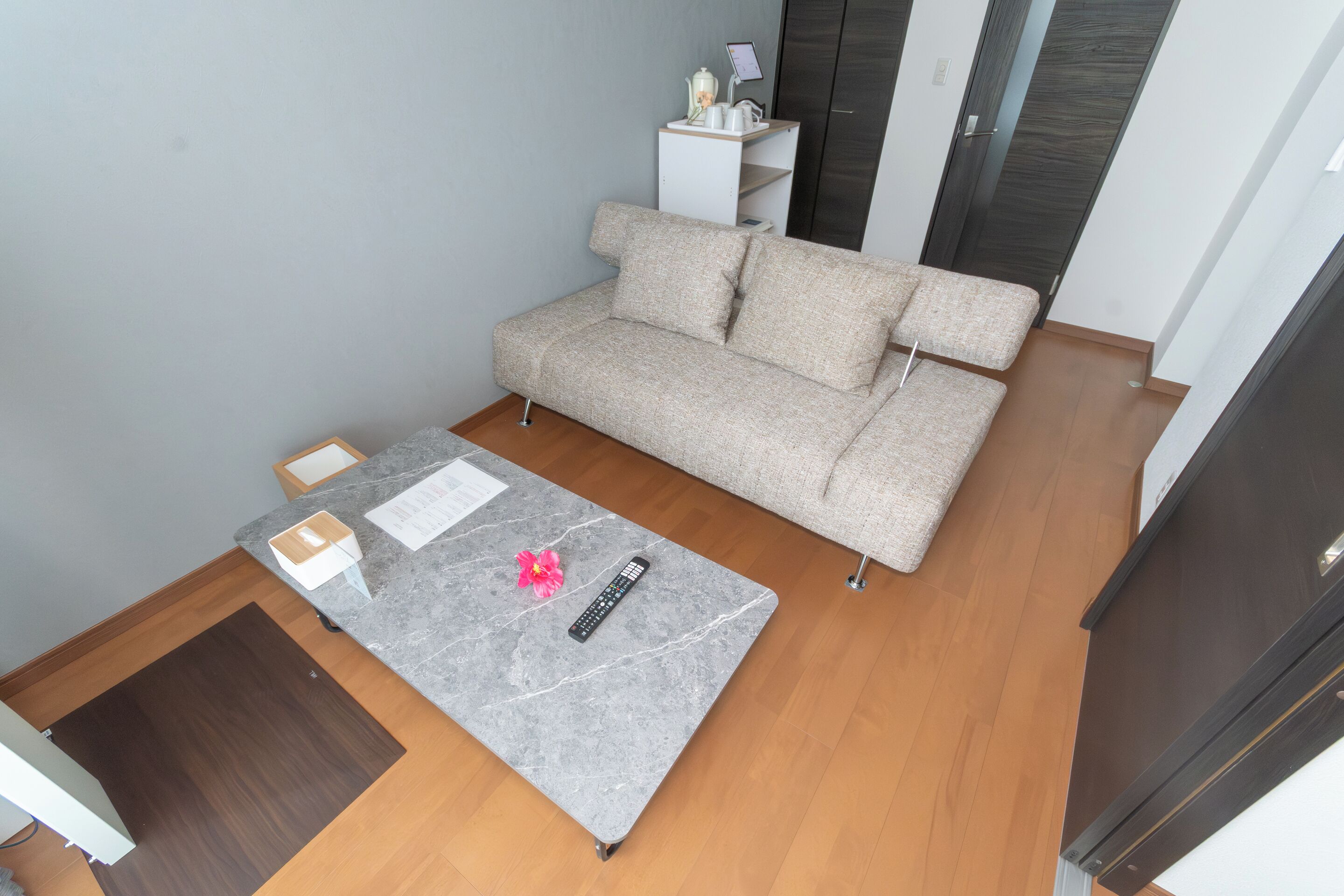 A room with a grey sofa, a small table with a remote control, and a white cabinet against the wall.