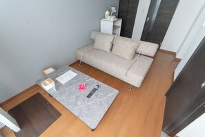 A room with a grey sofa, a small table with a remote control, and a white cabinet against the wall. - Kag.R Ohori 1 (Fukuoka)