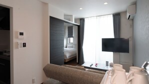 Ett hotellrum med en säng, en soffa, en tv, ett soffbord med muggar och ett fönster med gardiner.
