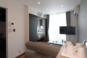 Ein Hotelzimmer mit Bett, Sofa, Fernseher, Couchtisch mit Tassen und einem Fenster mit Vorhängen.