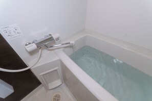 Eine Badewanne mit Duschkopf, Handlauf und Bedienfeld.
