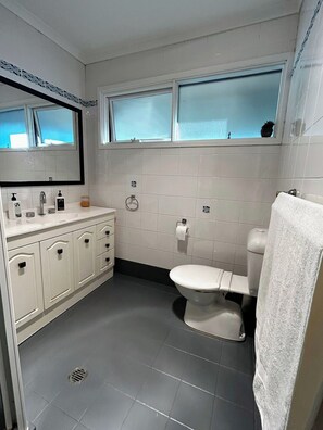 A bathroom with a toilet, sink, mirror, and window.