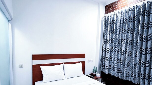 Une chambre d’hôtel avec un lit, une table de chevet, une fenêtre et un rideau orné d’un motif de feuilles.