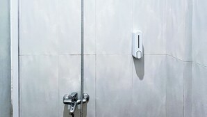 Une douche équipée d’un pommeau de douche à main, d’un panneau de commande fixé au mur et d’une sortie d’eau visible.