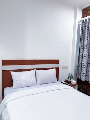 Una cama con ropa blanca, un cabecero de madera, una mesita de noche con un teléfono y una pared de ladrillo.