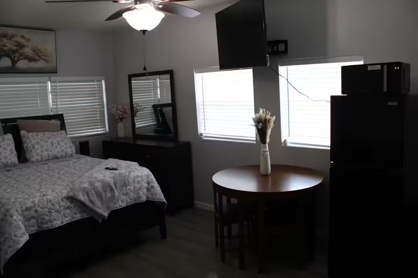 A bedroom with a bed, a dresser, a mirror, a ceiling fan, and a window with blinds.