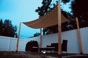A covered outdoor seating area with a barbecue grill, chairs, and string lights. - Raíces Del Bosque Studio. Peace and quiet…. (Lakeland)