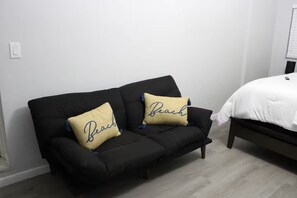 A black sofa with two beige pillows, a white bed with a white duvet, and a wooden floor. - Raíces Del Bosque Studio. Peace and quiet…. (Lakeland)