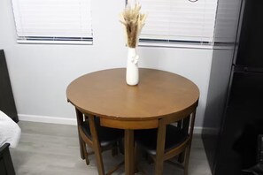 A round wooden dining table with four chairs, a white vase with dried flowers, and a window with blinds in the background. - Raíces Del Bosque Studio. Peace and quiet…. (Lakeland)