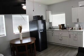 A modern kitchen with white cabinets, a black refrigerator, and a dining area with a wooden table and chairs. - Raíces Del Bosque Studio. Peace and quiet…. (Lakeland)