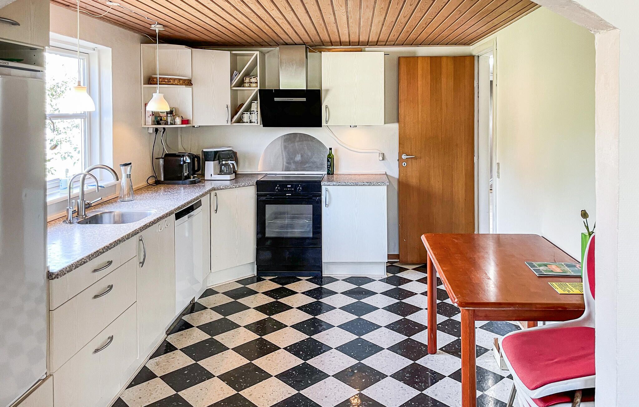 A compact kitchen with a checkered floor, a sink, a stove, and a dining table with a red chair.