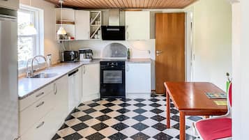 A compact kitchen with a checkered floor, a sink, a stove, and a dining table with a red chair.