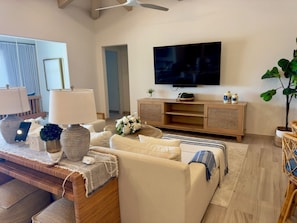 A living room with a sofa, a TV mounted on the wall, a wooden cabinet, and a plant. - Luxury 4BDR Casita 30 with Rooftop Lounge with Ocean View & private Jacuzzi (Diamante)