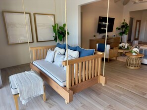 A room with a wooden swing bed, a bench, a television, and a dining area with a table and chairs. - Luxury 4BDR Casita 30 with Rooftop Lounge with Ocean View & private Jacuzzi (Diamante)