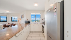 A modern kitchen with a view of the sea, a dining area, and a refrigerator with energy rating stickers. - Meridian unit 15 Kings Beach (Kings Beach)