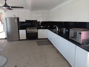 A kitchen with white cabinets, a stainless steel refrigerator, a gas stove, a microwave, and a ceiling fan.