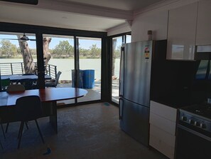 A kitchen with a refrigerator, stove, and dining table with chairs. - Pink Shack River Murray Getaway (Nildottie)