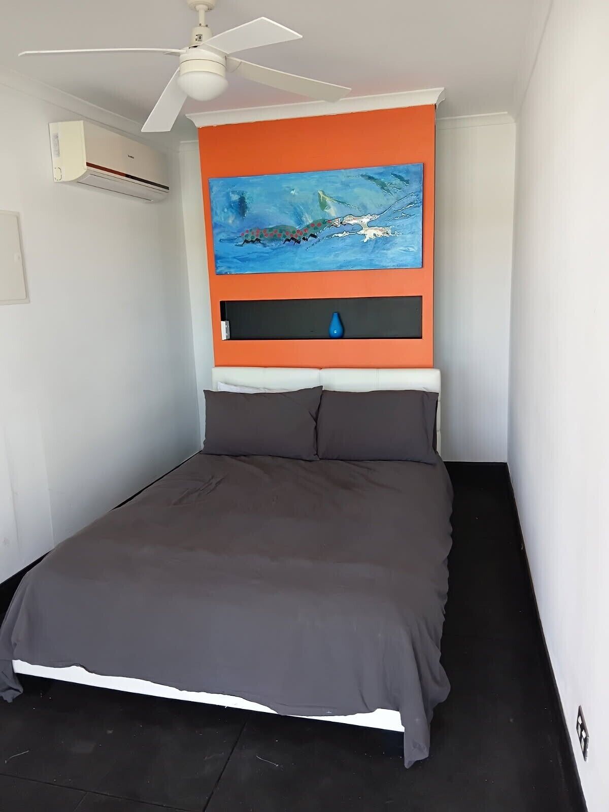 Une chambre à coucher avec un lit, un ventilateur de plafond, un appareil de climatisation, un tableau et un vase.