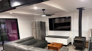 Una sala de estar moderna con un sofá modular, una mesa de centro de madera, un televisor empotrado, una estufa negra y un ventilador de techo.
