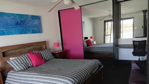 Un dormitorio con cama, escritorio, silla, espejo grande y ventilador de techo.