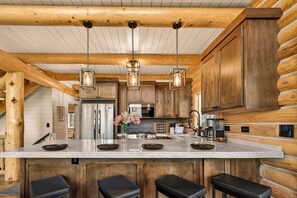 Une cuisine de style rustique, avec des murs en bois, un îlot en marbre, des luminaires suspendus et un réfrigérateur en acier inoxydable.