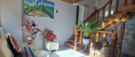 A living room with a wooden ceiling, a sofa, a painting, a staircase, and a marble floor.