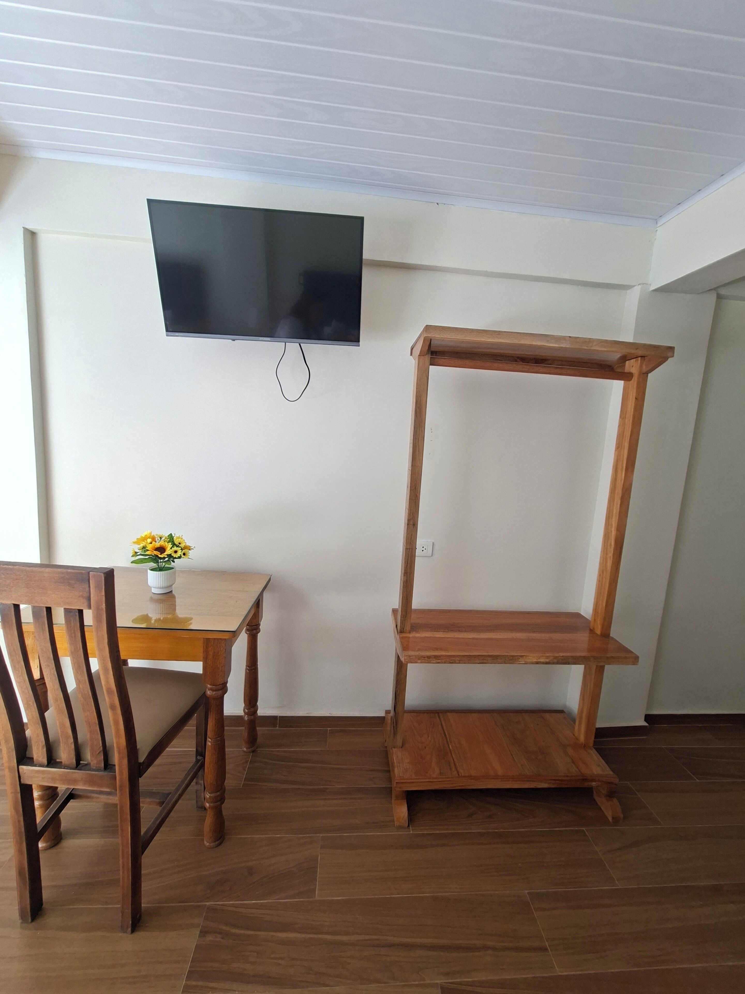 Una habitación con una mesa de comedor de madera, una silla, un televisor montado en la pared y una estantería de madera.