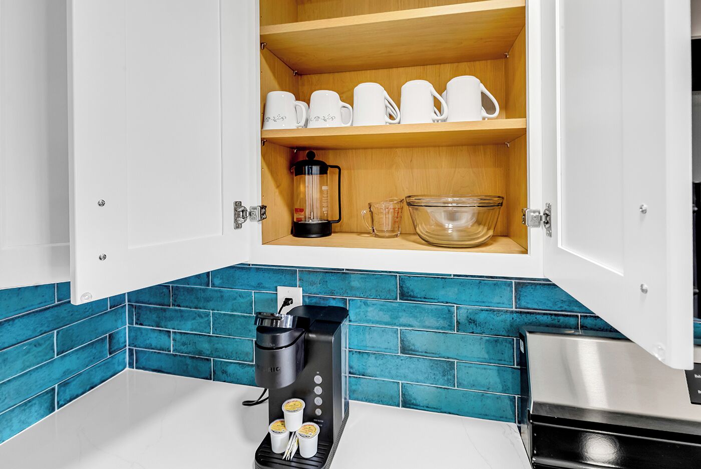 Una cucina con una macchina per il caffè, un frullatore e uno scaffale con tazze bianche.