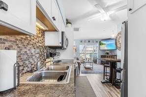 A modern kitchen with a brick backsplash, stainless steel appliances, and a dining area with a view. - Cozy coastal condo in St. James City with waterfront charm and easy island living. (Saint James City)