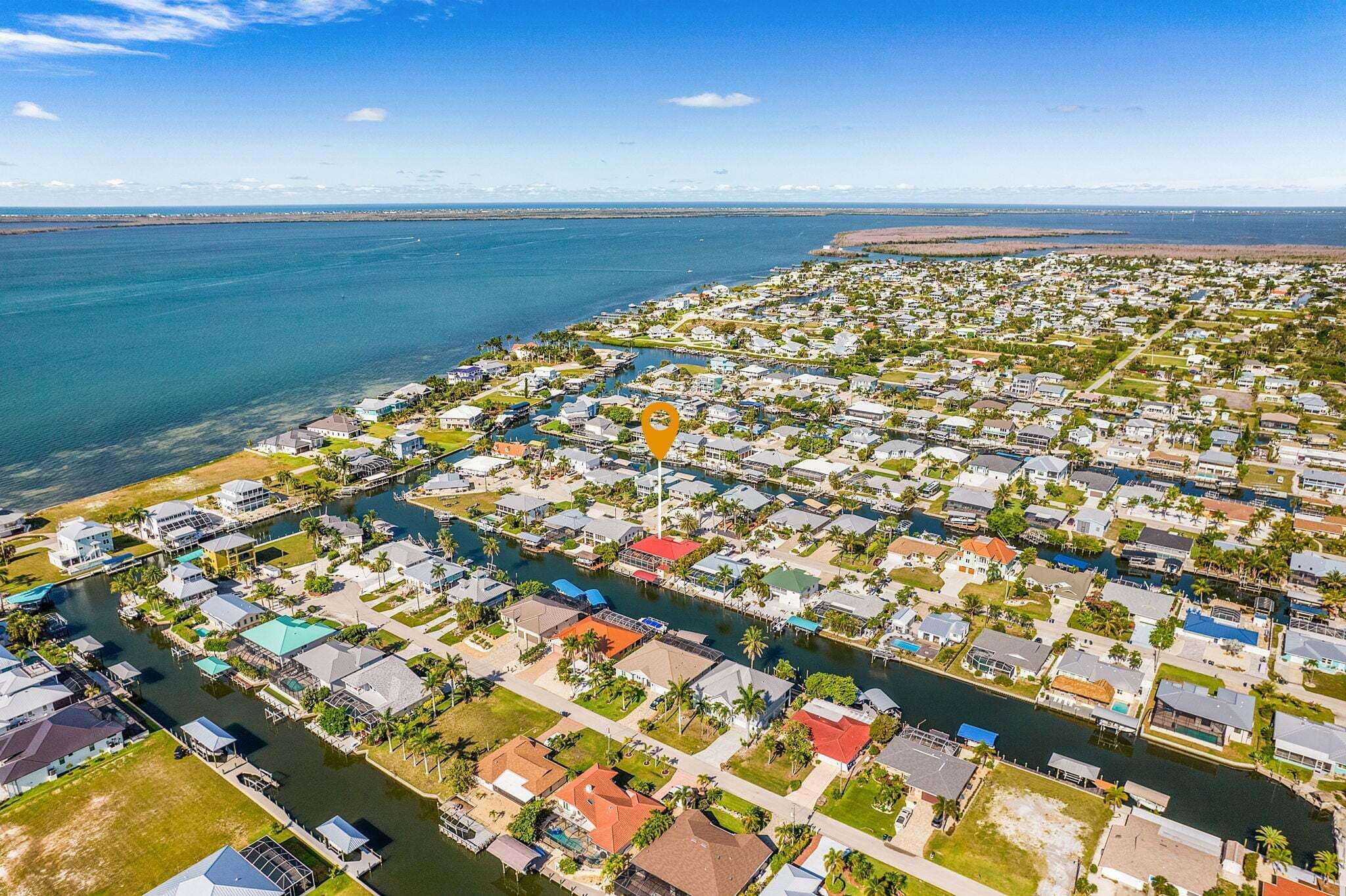 An aerial view of a coastal residential area with houses, a marina, and a clear view of the ocean.