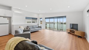 Una sala de estar moderna con un sofá, un mueble para televisión y un balcón con puertas de vidrio.