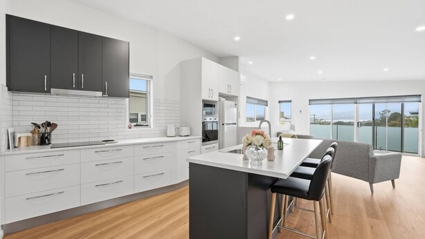 Una cocina moderna con armarios blancos, una isla central y un comedor con vistas.
