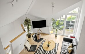 Ein großzügiger Wohnbereich mit einem großen Fenster, einem Flachbildfernseher, einer Couch, einem Couchtisch und zwei Zimmerpflanzen.