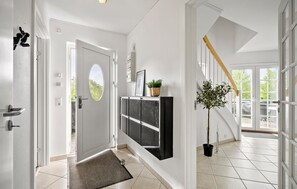 Ein Flur mit einer Tür, einem schwarzen Schrank, einem Blumentopf und einer Treppe, die zu einem Balkon führt.