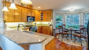 A kitchen with wooden cabinets, granite countertops, a built-in oven, and a dining area with a table and chairs.