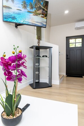 A room with a television mounted on the wall, a black door, and a plant with purple flowers on a white table.
