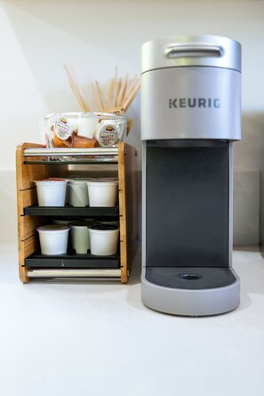 A coffee maker with a container of coffee pods and a wooden box with cups.