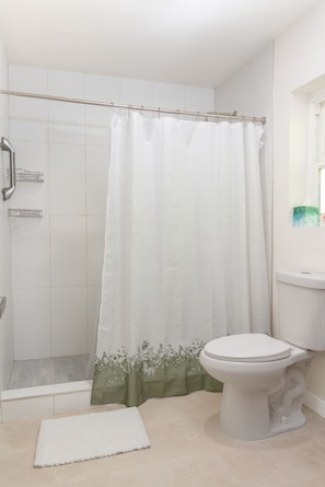Une salle de bain avec une douche, des toilettes et un tapis blanc.