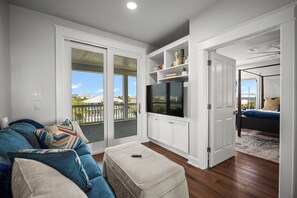 A living room with a sofa, ottoman, TV, and a sliding door leading to a balcony.