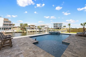 A swimming pool with lounge chairs, a dock with boats, and a marina.