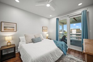 A bedroom with a bed, two bedside tables, a ceiling fan, and a view of the outside through a sliding glass door.