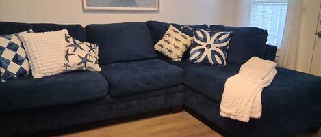 A dark blue sectional sofa with patterned cushions, a white throw blanket, and a wooden floor.