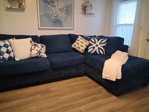 A dark blue sectional sofa with patterned cushions, a white throw blanket, and a wooden floor. - Coastal Escape in the Heart of Morehead City (Morehead City)